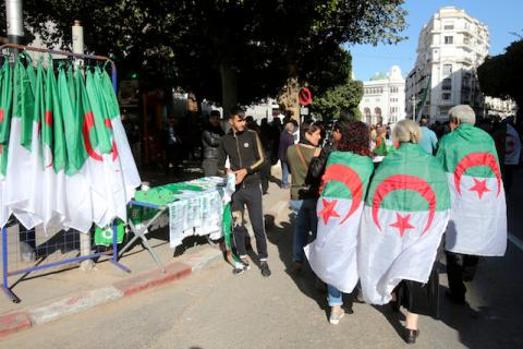 Demonstrators wearing national flags walk past a street vendor during a protest demanding a change of the power structure in Algiers, Algeria, January 24, 2020. PHOTO BY REUTERS/Ramzi Boudina