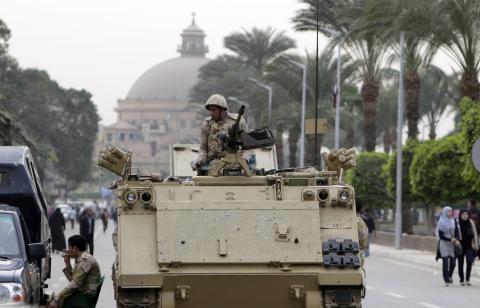 A soldier sits on guard atop an armoured personnel carrier (APC) at the main gate of the Cairo University