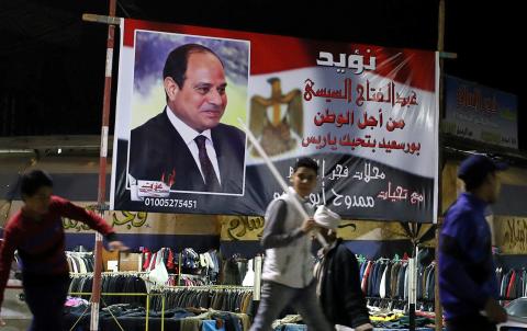 People walk in front of a banner supporting President Abdel Fattah al-Sisi's re-election hanging in a clothes market near the canal of Port Said, Egypt March 18, 2018. PHOTO BY REUTERS/Mohamed Abd El Ghany