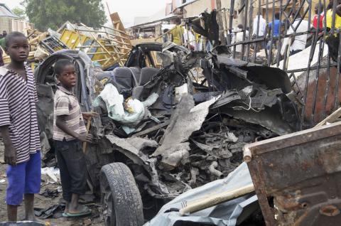 Two boys stand near the charred chassis of a vehicle after a bomb attack near a busy market area in Ajilari-Gomari near the city's airport, in Maiduguri