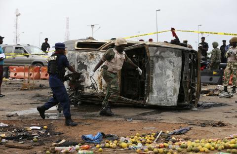 A soldier and a paramilitary officer help to move part of a damaged car at the scene of a car bomb attack in Nyanya, Abuja