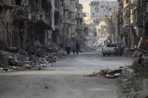 A Free Syrian Army fighter walks with his family through damage and debris along a street Deir al-Zor, eastern Syria