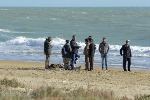 People stand next to the dead body of a migrant on the beach of Siculiana, in Western Sicily, Italy, February 19, 2016. PHOTO BY REUTERS/Guglielmo Mangiapane