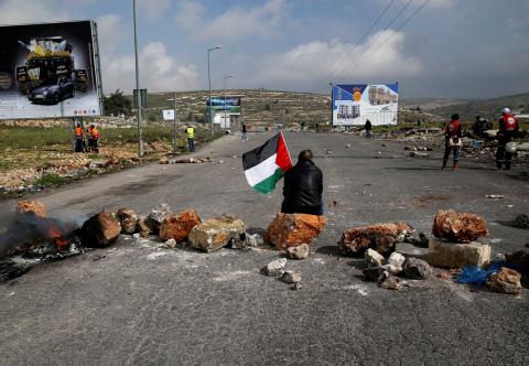 A demonstrator holds a Palestinian flag as he sits during clashes with Israeli troops near the Jewish settlement of Beit El, near Ramallah in the occupied West Bank, February 23, 2018. PHOTO BY REUTERS/Ammar Awad