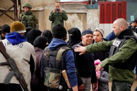 A Syrian security personnel (R) and Russian soldiers (back) monitor as rebel fighters and their families evacuate the besieged Waer district in the central Syrian city of Homs, after an agreement was reached between rebels and Syria's army, March 18, 2017. PHOTO BY REUTERS/Omar Sanadiki