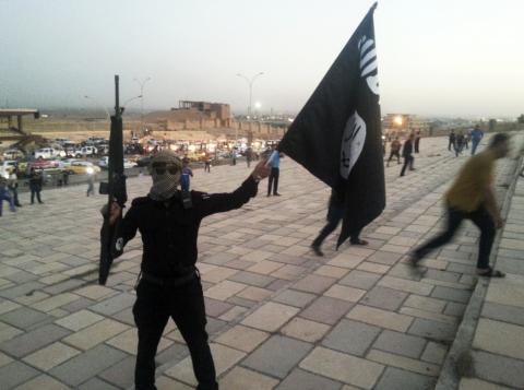 A fighter of the Islamic State of Iraq and the Levant (ISIL) holds an ISIL flag and a weapon on a street in the city of Mosul