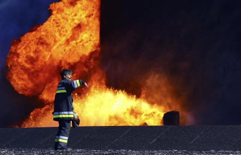 A firefighter stands near the fire of a storage oil tank at the port of Es Sider in Ras Lanuf, December 29, 2014. PHOTO BY REUTERS/Stringer