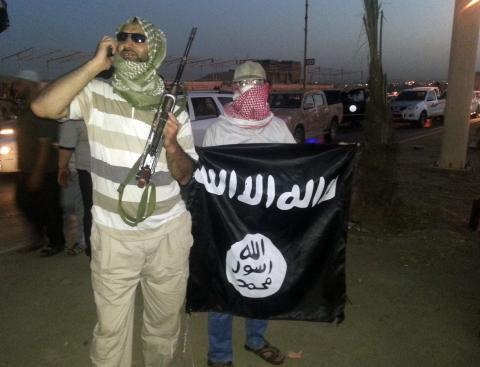 A fighter of the Islamic State of Iraq and the Levant (ISIL) holds a weapon while another holds a flag in the city of Mosul