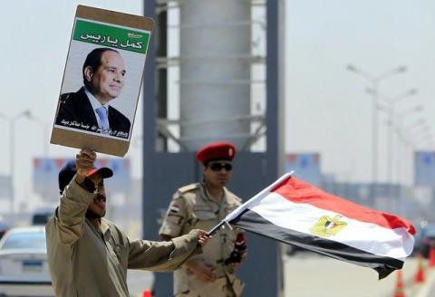 A man carrying a portrait of Egyptian President Abdel Fattah al-Sisi and an Egyptian flag stands next to a soldier during the funeral of Egyptian public prosecutor Hisham Barakat, on the second anniversary of the June 30 protests in Cairo, Egypt, June 30, 2015. PHOTO BY REUTERS/Mohamed Abd El Ghany