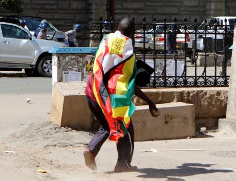 A man with a Zimbabwean flag wrapped around him throws stones at police officers during a protest against President Robert Mugabe's government's handling of the economy in Harare, Zimbabwe, August 3, 2016. PHOTO BY REUTERS/Philimon Bulawayo