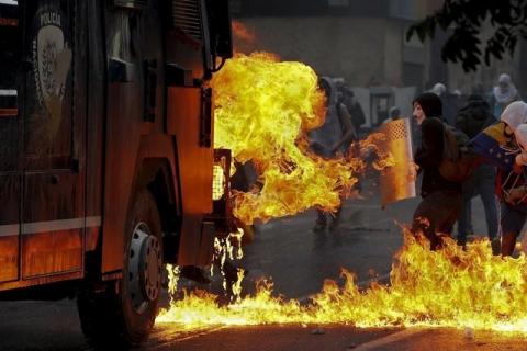 An anti-government protester wearing a Guy Fawkes mask stands with a shield near flames from molotov cocktails thrown at a water cannon by anti-government protesters during riots in Caracas, April 20, 2014. PHOTO BY REUTERS/Jorge Silva