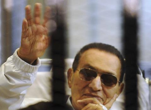 Former Egyptian President Hosni Mubarak waves to his supporters inside a cage in a courtroom