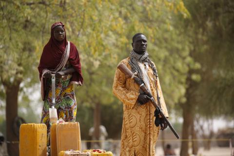 A member of a civilian vigilante group holds a hunting rifle while a woman pumps water into jerrycans in Kerawa, Cameroon, March 16, 2016. Kerawa is on the border with Nigeria and is subject to frequent Boko Haram attacks. After watching its influence spread during a six-year campaign that has killed around 15,000 people according to the U.S. military, Nigeria has now united with its neighbours to stamp out Boko Haram. PHOTO BY REUTERS/Joe Penney