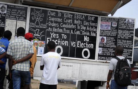 Bystanders read the headlines illustrating the battle over the holding of elections in Liberia amid the Ebola crisis at a street side chalkboard newspaper in Monrovia, December 2, 2014. PHOTO BY REUTERS/James Giahyue