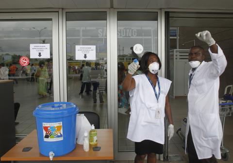 Health workers wearing protective masks and gloves gesture as they talk at the Felix Houphouet Boigny international airport in Abidjan