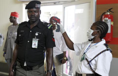 An immigration officer uses an infra-red laser thermometer to examine a policeman on his arrival at Nnamdi Azikiwe International Airport in Abuja