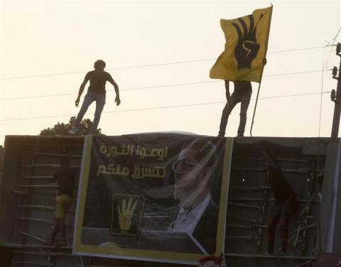 Members of the Muslim Brotherhood and supporters of ousted Egyptian President Mohamed Mursi climb a structure to hang up a poster of Mursi during a protest