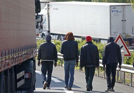 Migrants walk near trucks blocked on a road which leads to the Channel Tunnel terminal in Coquelles near Calais, northern France, July 1, 2015. PHOTO BY REUTERS/Vincent Kessler