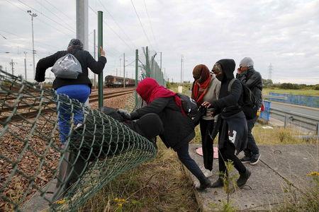 Migrants make their way across a fence near near train tracks as they attempt to access the Channel Tunnel in Frethun, near Calais, France, July 29, 2015. PHOTO BY REUTERS/Pascal Rossignol