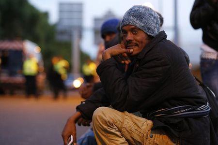 Migrants sit and gather as French gendarmes wearing security vests secure a road at nightfall in Coquelles, near Calais, France, July 30, 2015. PHOTO BY REUTERS/Pascal Rossignol