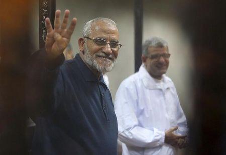 Muslim Brotherhood's Supreme Guide Mohamed Badie (L) flashes the Rabaa sign as he stands behind bars during his trial with ousted Egyptian President Mohamed Mursi and other leaders of the brotherhood at a court in the police academy on the outskirts of Cairo, December 14, 2014. PHOTO BY REUTERS/Asmaa Waguih