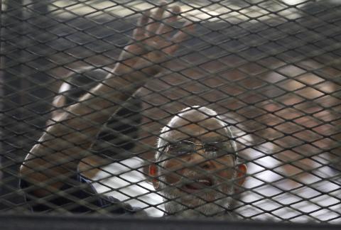 Muslim Brotherhood's General Guide Mohamed Badie shouts slogans and gestures the four-fingered "Rabaa" hand symbol from the defendant's cage in a courtroom in Cairo