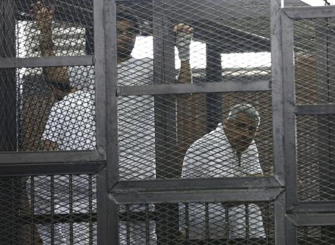 Mohamed Fahmy (R), stands behind bars as he waits to listen the ruling at a court in Cairo