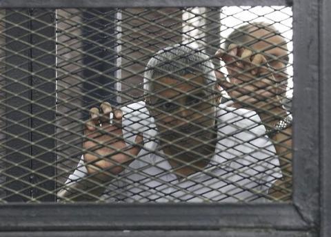 Mohamed Fahmy stands behind bars as he waits to listen the ruling at a court in Cairo, June 23, 2014. PHOTO BY REUTERS/Asmaa Waguih