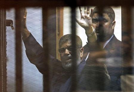 Deposed Egyptian President Mohamed Mursi greets his lawyers and people from behind bars after his verdict at a court on the outskirts of Cairo, June 16, 2015. PHOTO BY REUTERS/Asmaa Waguih