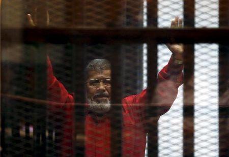 Deposed President Mohamed Mursi greets his lawyers and people from behind bars at a court wearing the red uniform of a prisoner sentenced to death, during his court appearance with Muslim Brotherhood members on the outskirts of Cairo, Egypt, June 21, 2015. PHOTO BY REUTERS/Amr Abdallah Dalsh