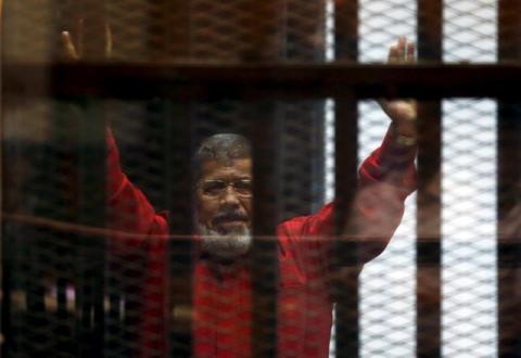 Egypt's deposed president Mohamed Mursi greets his lawyers and people from behind bars at a court wearing the red uniform of a prisoner sentenced to death, during his court appearance with Muslim Brotherhood members on the outskirts of Cairo, Egypt, June 21, 2015. PHOTO BY REUTERS/Amr Abdallah Dalsh