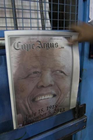 A man reaches for a copy of recently printed newspaper paying tribute to forrmer South Africa's former President Nelson Mandela at a printing press in the early hours of the morning in Cape Town