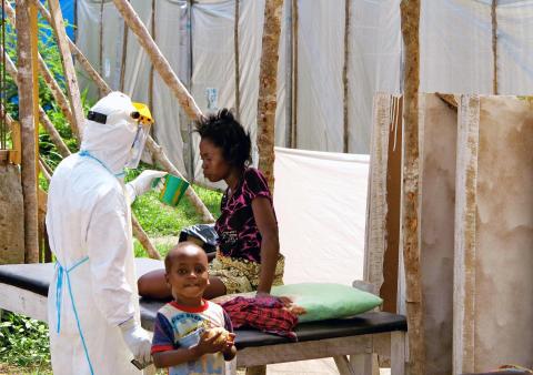 A health worker, wearing head-to-toe protective gear, offers water to a woman with Ebola, at a treatment centre for infected persons, as a young boy stands nearby in Kenema Government Hospital, in Kenema, Eastern Province, Sierra Leone