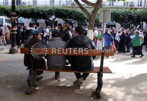 People sit on a bench as protesters demanding a change of the power structure march in Algiers, Algeria, January 21, 2020. PHOTO BY REUTERS/Ramzi Boudina