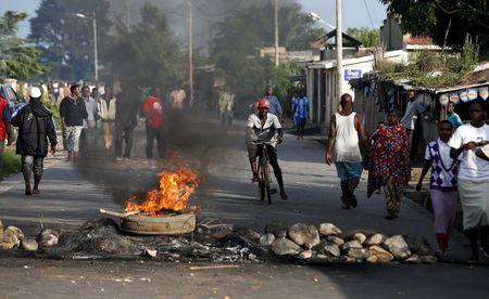 People walk next to a burning barricade during a protest against President Pierre Nkurunziza's decision to run for a third term, in Buterere neighbourhood of Bujumbura, Burundi, May 13, 2015. PHOTO BY REUTERS/Goran Tomasevic