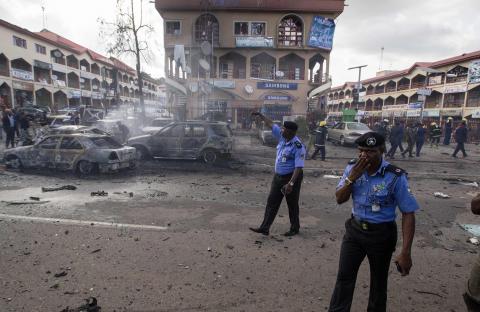 Policemen walk towards burnt vehicles at the scene of a blast at a business district in Abuja