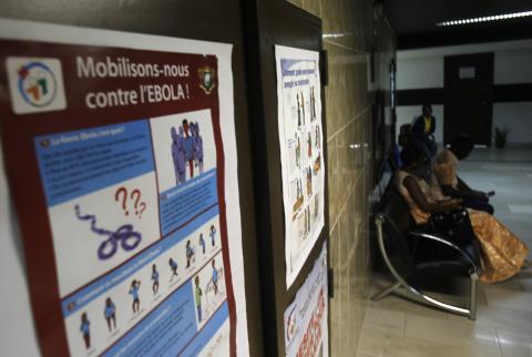 People sit near a poster with a government message against Ebola, at the health minister's office in Abidjan