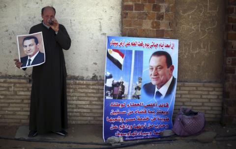 Reda Shehata, a supporter of Egypt's former president Hosni Mubarak drinks tea as he holds his poster, outside the police academy, where Mubarak's trial will take place, in Cairo