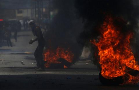 A Palestinian protester stands next to burning tyres during clashes with Israeli troops near Qalandiya checkpoint near the West Bank city of Ramallah, July 21, 2017. PHOTO BY REUTERS/Mohamad Torokman