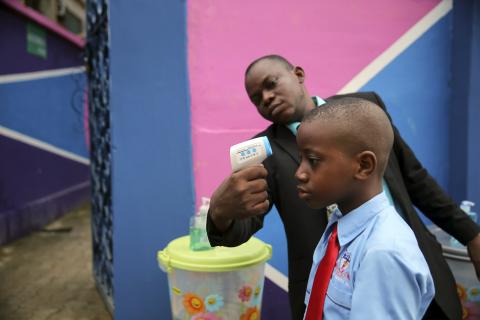 A school official takes a pupil's temperature using an infrared digital laser thermometer in front of the school premises, at the resumption of private schools, in Lagos, Nigeria