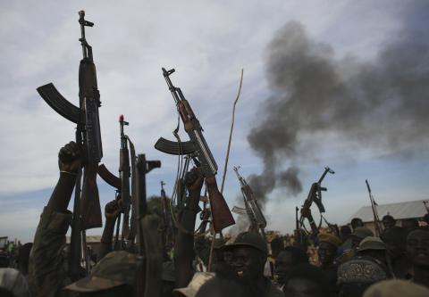 Rebel fighters hold up their rifles as they walk in front of a bushfire in a rebel controlled territory in Upper Nile State