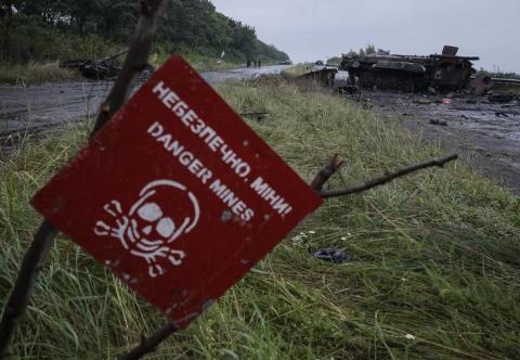 A destroyed military vehicle is seen near a landmine warning sign