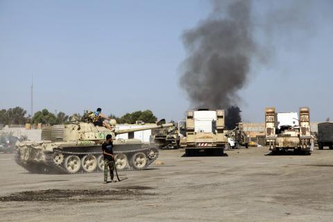 Smoke is seen rising from the Brigade Qaqaa headquarters, a former Libyan Army camp known as Camp 7 April, behind members of the Libya Shield, following clashes between rival militias at the Sawani road district in Tripoli