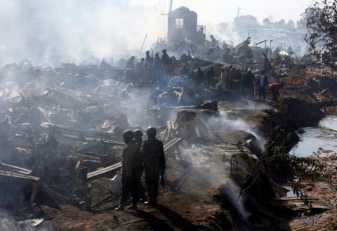 Traders and riot police are seen at the smouldering scene of fire that gutted down the timber dealership of the Gikomba market and nearby homes in central Nairobi, Kenya, June 28, 2018. PHOTO BY REUTERS/Thomas Mukoya