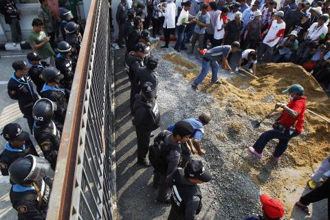 Government supporters begin to build a wall at the gates of the National Anti-Corruption Commission (NACC) office as policemen guard it in Nonthaburi province, on the outskirts of Bangkok