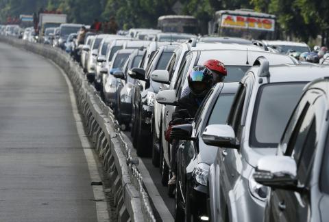 People on a motorcycle look on while in between other vehicles in a gridlocked street in Jakarta