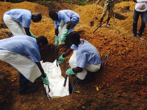 Volunteers lower a corpse, which is prepared with safe burial practices to ensure it does not pose a health risk to others and stop the chain of person-to-person transmission of Ebola, into a grave in Kailahun