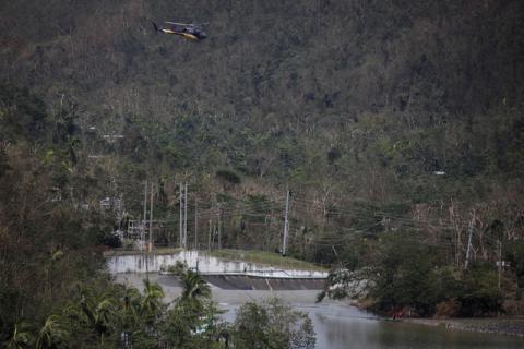 People look at water flowing over the road as a helicopter flies over them at the dam of the Guajataca lake. PHOTO BY REUTERS/Carlos Garcia Rawlins