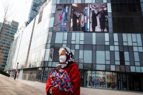 A woman wearing a face mask walks past a screen showing a video about protective measures against the new coronavirus in Beijing, China, February 26, 2020. PHOTO BY REUTERS/Thomas Peter