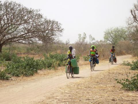 Women cycle with water tins towards the village of Bagare, Passore province, northern Burkina Faso, March 30, 2016. PHOTO BY REUTERS/Zoe Tabary